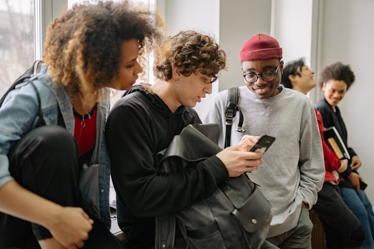A group of diverse college students hanging out indoors and using a smartphone together.
